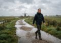 Man wandelt stevig door de polder in lichte herfstregen